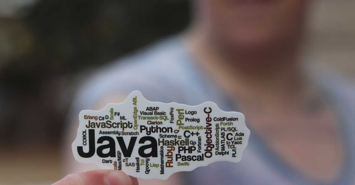 Close-up of a person holding a sticker with various programming languages listed on it.